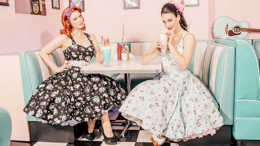 Dos chicas lucen vestidos pin up en una cafetería estilo años 50 mientras escuchan música rockabilly